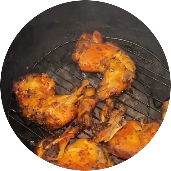 Potongan ayam berbumbu rempah dipanggang di atas jaring dalam tungku gerabah, dilihat dari atas