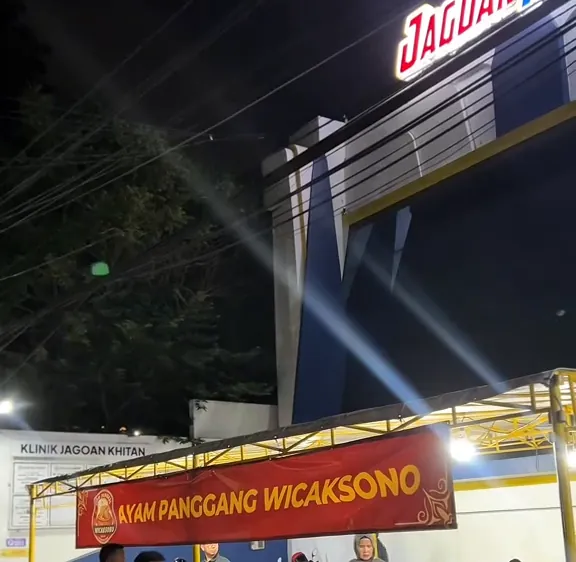 Tampak depan warung Ayam Panggang Wicaksono di bawah papan nama Klinik Jagoan Khitan pada malam hari