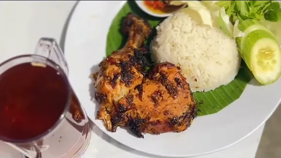 Ayam panggang dengan nasi, timun, lalapan, dan segelas teh di meja putih